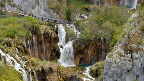 Panoramic-view-of-Plitvice-Lakes-National-Park-in-Croatia,-tourists-walking-on-wooden-bridge-pathway