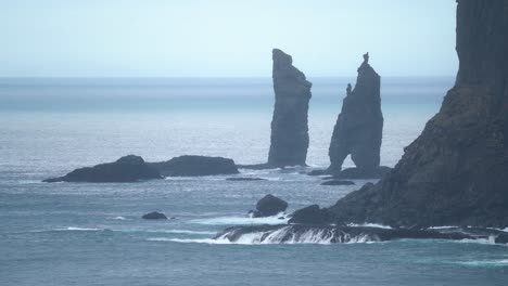 Wide-shot-showing-Risinn-og-Kerlingin-sea-stacks-on-Streymoy-Island-with-crashing-waves---slow-motion