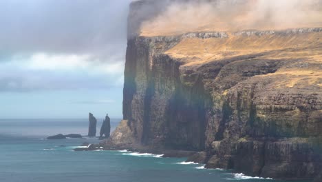Panorama-view-of-beautiful-rainbow-shining-in-front-of-massive-coastline-and-Risin-og-Kellingin-sea-stacks,-in-background-Streymoy-Island,-Faroe-Islands