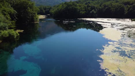 Drone-shot-of-the-Blue-Eye-in-Albania---drone-is-following-the-river-flow,-showing-the-sun-reflection-in-the-clear-water