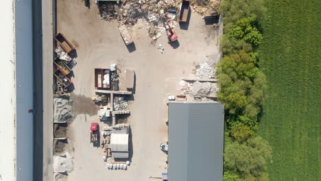 Top-down-aerial-of-busy-metal-recycling-center---drone-flying-backwards-and-revealing-industrious-site