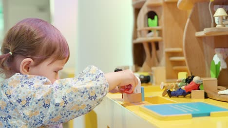 Koreanisch-ukrainisches-2-jähriges-Kleinkind,-Das-Mit-Spielzeugfiguren-Im-Puppenhaus-Spielt,-Das-Am-Schreibtisch-Sitzt