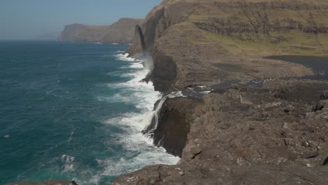 View-Of-Bosdalafossur-Waterfall-With-Geitaskoradrangur-Sea-Stack-At-The-Background-In-Faroe-Islands
