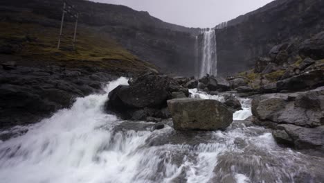 Zoom-out-shot-of-massive-crashing-Fossarfoss-waterfall-on-Streymoy-Island-during-cloudy-day---Highest-waterfall-on-Faroe-Islands