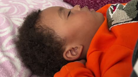 Close-side-view-of-an-exotic-african-european-two-year-old-child-sleeping-deeply-in-his-bed