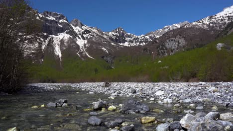 Calming-panorama,-magnificent-alpine-landscape-with-snow-capped-mountains-and-stream-with-crystal-clear-water
