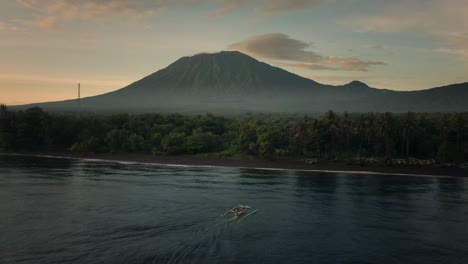 Fishing-boat-arriving-at-moody-tropical-shore-of-Bali-with-grand-Mount-Agung,-Kubu-Beach,-aerial