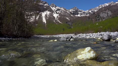 Sauberes-Wasser,-Das-Durch-Steine-Im-Flussbett-Mit-Hohen-Alpenbergen-Im-Hintergrund-Fließt