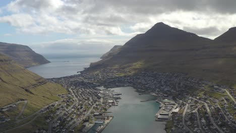 Drone-backwards-flight-showing-bay-and-coastal-city-of-Klaksvik-on-Faroe-Island-during-sunny-and-cloudy-day---Housing-area-and-architecture-around-river-bay-on-Bordoy-Island