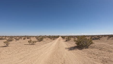 Driver-point-of-view-driving-along-a-dirt-road-in-the-barren-Mojave-Desert's-arid-landscape