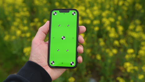 Landwirt,-Der-Ein-Smartphone-Mit-Grünem-Bildschirm-Auf-Einem-Blühenden-Rapsfeld-Hält