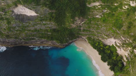 Secluded-tropical-beach-with-tall-cliffs-on-Nusa-Penida-island,-aerial