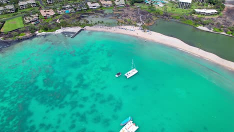Sailboats-anchored-in-the-Anaehoomalu-Bay-not-far-from-the-white-sand-beach---aerial-pull-back-reveal