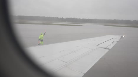 A-male-wing-walker-guides-plane-with-orange-batons-on-the-tarmac-runway-before-takeoff---as-seen-from-inside-the-commercial-airplane