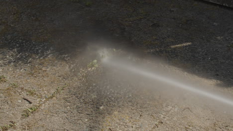 Powerful-water-jet-from-pressure-washer-being-sprayed-on-dirty-garden-tiles
