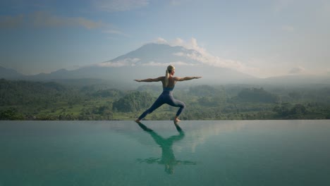 Woman-lunging-into-Warrior-Yoga-Pose-on-edge-of-infinity-pool-with-mount-Agung-at-sunrise