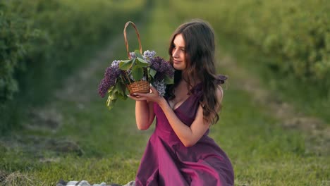 Portrait-of-a-beautiful-young-woman-in-a-field-in-a-purple-dress-with-a-basket-of-lilac-flowers