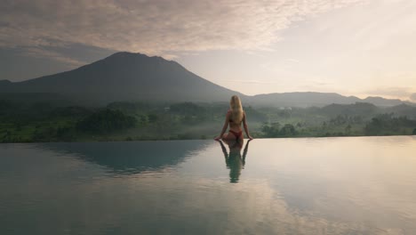 Fit-woman-in-bikini-on-pool-edge-looking-at-magical-sunrise-with-Volcano-Agung