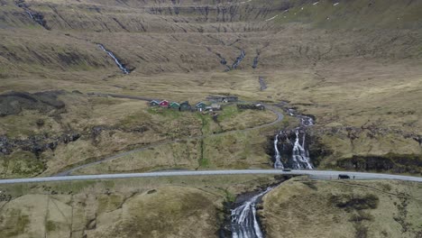 Aerial-view-of-idyllic-waterfall-flowing-downhill-in-Fuglafjörður-on-Eysturoy-Island,Faroe-Islands---Spectacular-drone-shot-with-driving-cars-on-mountain-road