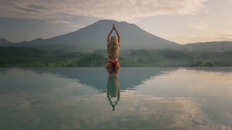 Woman-in-bikini-with-hourglass-figure-sitting-on-infinity-pool-edge-yoga-salute-to-Mount-Agung