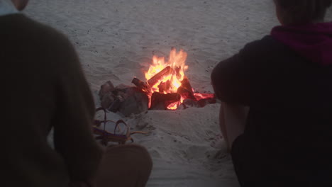 People-Sitting-On-Sand-And-Warming-Themselves-By-The-Bonfire-At-The-Beach-In-St