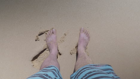 Ein-Blick-Auf-Die-Beine-Des-Mannes,-Der-Im-Sand-An-Einem-Strand-Steht,-Während-Der-Wind-Weht