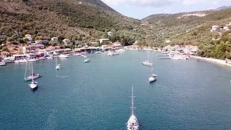 Boat-Sails-to-Harbour-at-Mikros-Gialos,-Lefkada,-Greece---Aerial