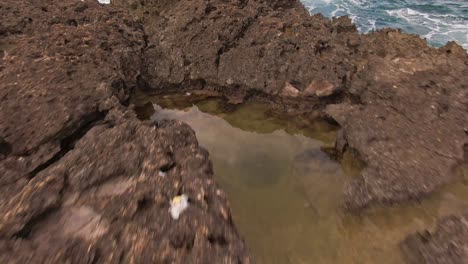 Low-angle-dolly-forward-of-rock-formation-at-Hawaiian-beach