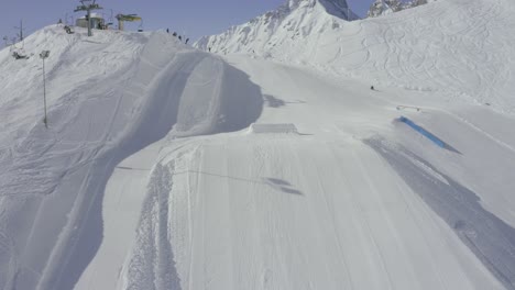Snowboarder-jumping-in-terrain-park,-Nordkette-ski-resort-above-Innsbruck,-Skyline-park-Austrian-Alps-ski-resort-drone-aerial-view