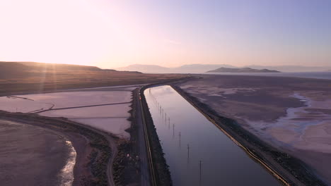Cinematic-sunrise-drone-shot-of-pink-salt-lake-in-Utah-and-oncoming-train