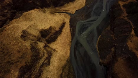 Aerial-view-of-a-river-flowing-through-Iceland-highlands-on-volcanic-black-sand
