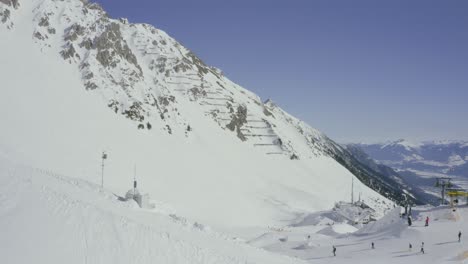 Flyover-of-Nordkette-ski-resort-above-Innsbruck,-Skyline-terrain-park-reveal-over-snowy-ridge-with-chairlift-,-Austrian-Alps-drone-pan-down