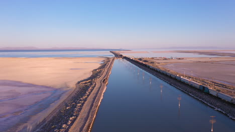 Drone-flys-next-to-long-freight-train-crossing-the-causeway-over-the-Great-Salt-Lake-in-Utah,-USA