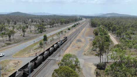 Empty-coal-train-running-on-railway-parallel-to-road,-Bajool-in-Queensland,-Australia