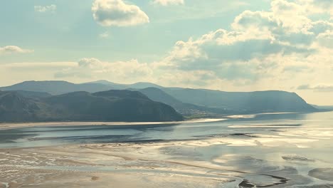 Slowly-rising-water-after-low-tide-in-the-tidal-area-off-the-coast-of-Wales-with-the-mountains-of-the-mountainous-landscape-in-the-background-lit-by-the-sun-between-the-clouds