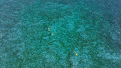 Perfect-turquoise-blue-sea-water-with-three-people-in-yellow-kayaks,-summer-activity,-aerial