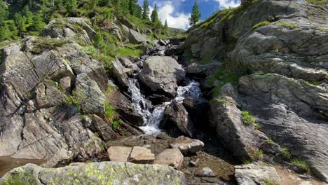Small-river-in-the-alps-between-rocks-and-with-bubbling-water,-flowing-down-from-a-mountain-in-Austria