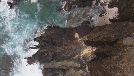 Overhead-view-of-waves-on-rocky-beach-cliffs-tracking-forward