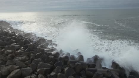 Wave-crash-into-rocks,-frothing-sea-water-streams-down-rock-face,-turbulent-ocean