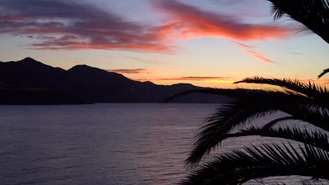 Schöner-Sonnenuntergang-über-Dem-Ozean-Mit-Palmblättern-Und-Bergsilhouette
