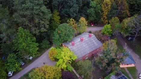 Aerial-top-down-dolly-out-over-modern-house-hidden-between-autumnal-colorful-woods-at-daytime,-cars-parked