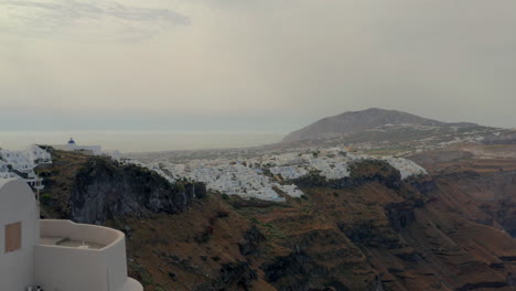 Aerial:-Panoramic-view-of-Fira-in-Santorini,-Greece-during-cloudy-sunrise