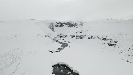 Luftaufnahme-Eines-Mannes,-Der-Auf-Schneebedeckten-Bergen-In-Richtung-Svöðufoss-Wasserfall-Auf-Der-Halbinsel-Snæfellsnes,-Island,-Wandert