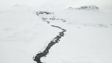Hombre-Caminando-En-Un-Frío-Día-De-Invierno-Hacia-La-Cascada-Svodufoss-En-Islandia