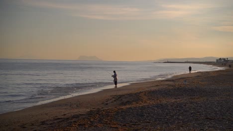 Two-fisherman-standing-on-beach-during-sunset-and-Gibraltar-in-distance