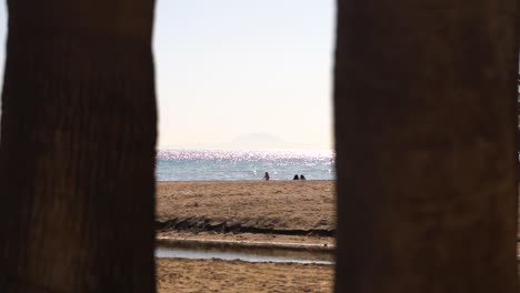Interesting-beach-view-in-between-two-trees-towards-people-and-ocean-in-slow-motion