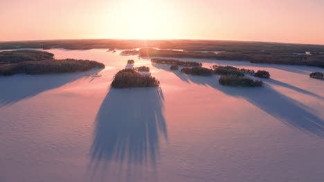 Aerial-drone-shot-of-sunset-over-untouched-icy-lake-with-long-shadows-of-small-islands