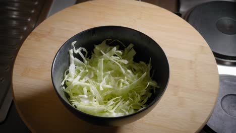 Male-Hand-is-Adding-and-Removing-a-Bowl-of-Sliced-Cabbage-From-a-Table,-Cooking-Scrambled-Eggs