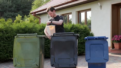 Caucasian-man-sorting-litter-into-trash-bins-at-backyard