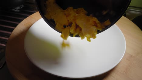 Person-is-pouring-scrambled-eggs-from-a-frying-pan-onto-a-plate
